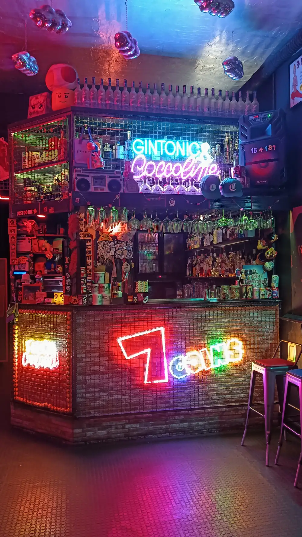 Il bancone del 7COINS: insegna 7COINS al neon, la scritta Gintonic & Coccoline e le nuvole di palle da discoteca sul soffitto